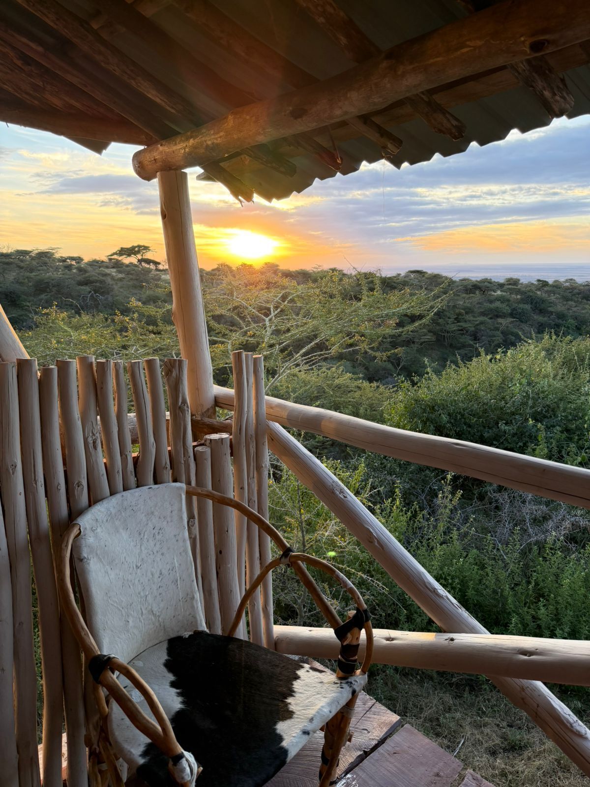 Una silla de madera con cojín blanco y negro, barandilla de madera y vista al atardecer sobre un paisaje.