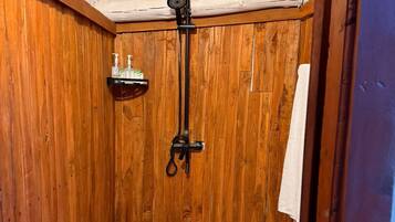 Ein Duschraum mit Holzwandverkleidung, ausgestattet mit einem eingebauten Ablagebereich für Toilettenartikel, einer Duschbrause und einem Handtuchhalter.