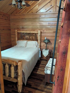 A wooden cabin bedroom with a bed, a nightstand, a lamp, and a ceiling fan. - Luxury Craftsman 1-bedroom cabin in SERENE beauty with AC, high end kitchen/bath (Ava)