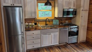 A kitchen with wooden cabinets, stainless steel appliances, a window with a view, and a hanging light fixture. - Luxury Craftsman 1-bedroom cabin in SERENE beauty with AC, high end kitchen/bath (Ava)