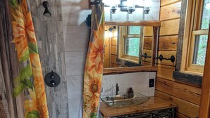 A wooden cabin bathroom with a shower curtain, a sink, a mirror, and a toilet. - Luxury Craftsman 1-bedroom cabin in SERENE beauty with AC, high end kitchen/bath (Ava)