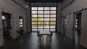 Een ruime kamer met een groot raam, een tafel met stoelen en een deur.
