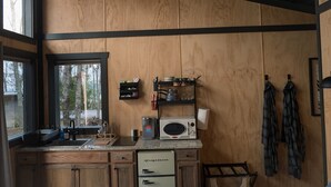 Een keuken met houten kastjes, een koffiezetapparaat, een magnetron en een raam met uitzicht op bomen.