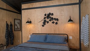 Een slaapkamer met een bed, twee wandlampen, een kunstwerk aan de muur, en een handdoek.