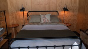 Ein Bett mit Metallgestell, zwei Nachttischlampen, ein Kissen mit rotem Muster und eine Holzwand.