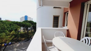 Un balcón con una mesa y sillas, una ventana y vistas a árboles y edificios.