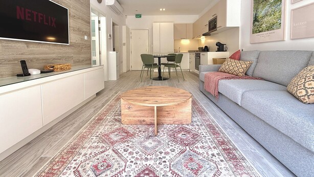 A modern living room with a flat-screen TV, a sofa, a coffee table, and a patterned rug.