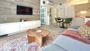A modern living room with a flat-screen TV, a wooden coffee table, a sofa, and a dining area with chairs.