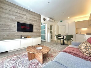 Ett modernt vardagsrum med en platt-TV, ett soffbord i trä, en soffa och en matplats med stolar.