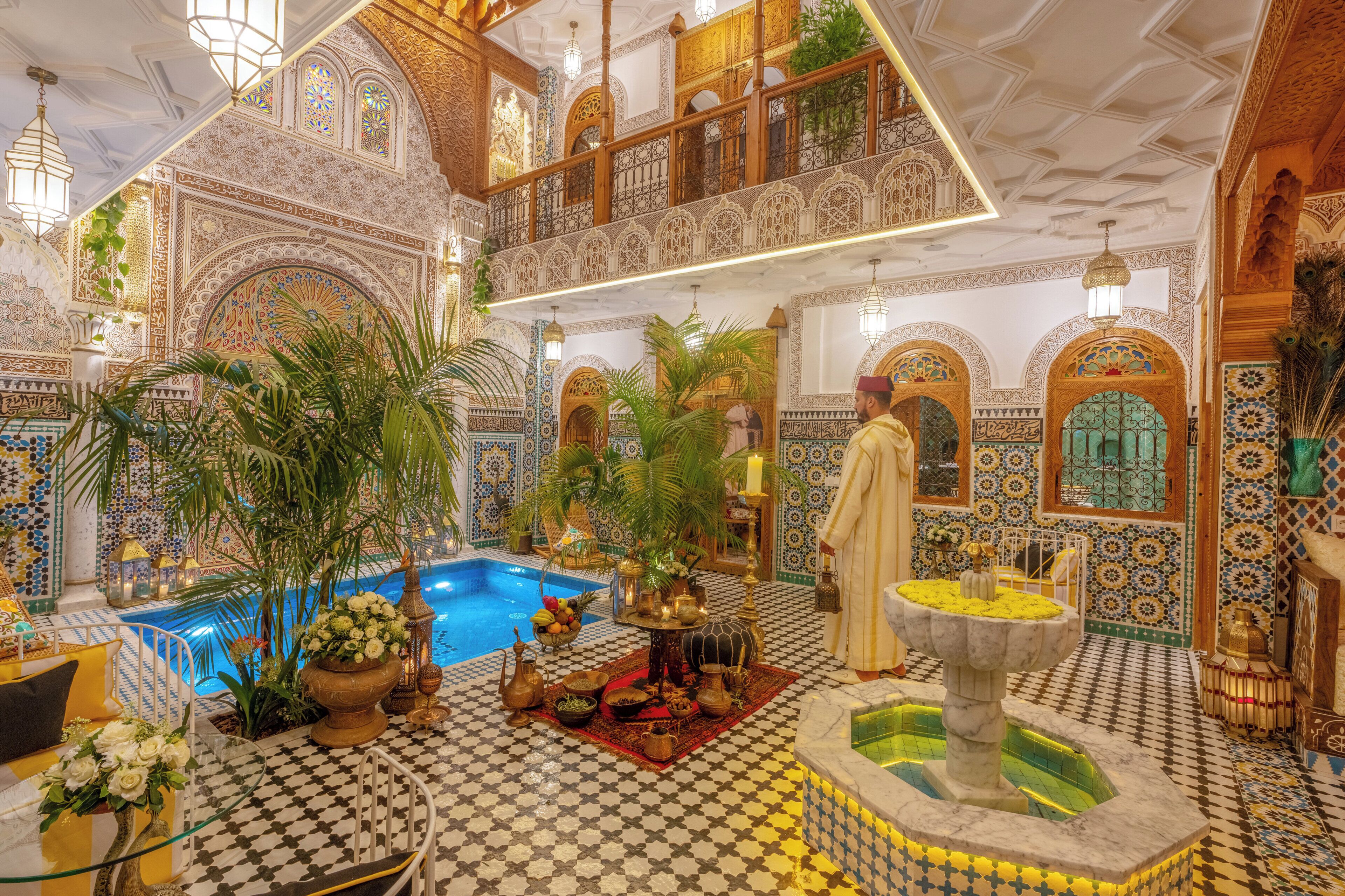 A luxurious interior with a pool, ornate decor, and a man in traditional attire.