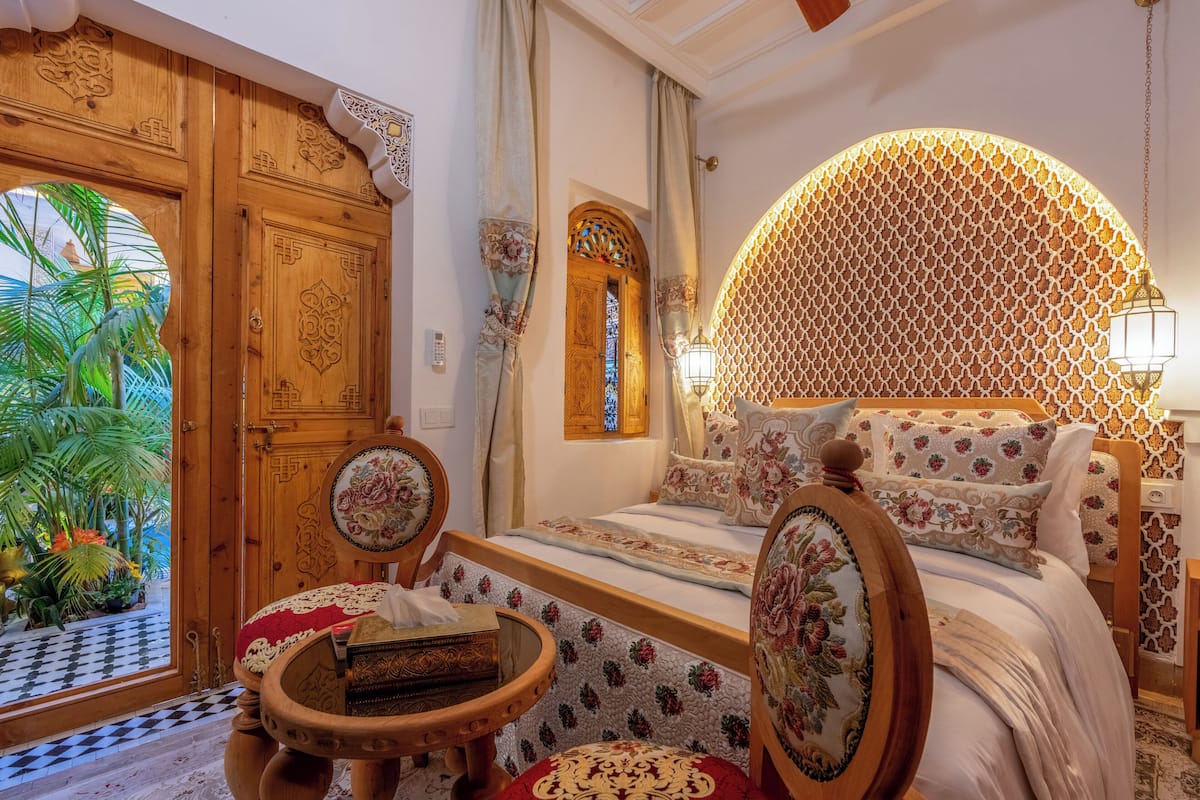 Una habitación con una cama, una puerta de madera, una mesita y vistas a palmeras.