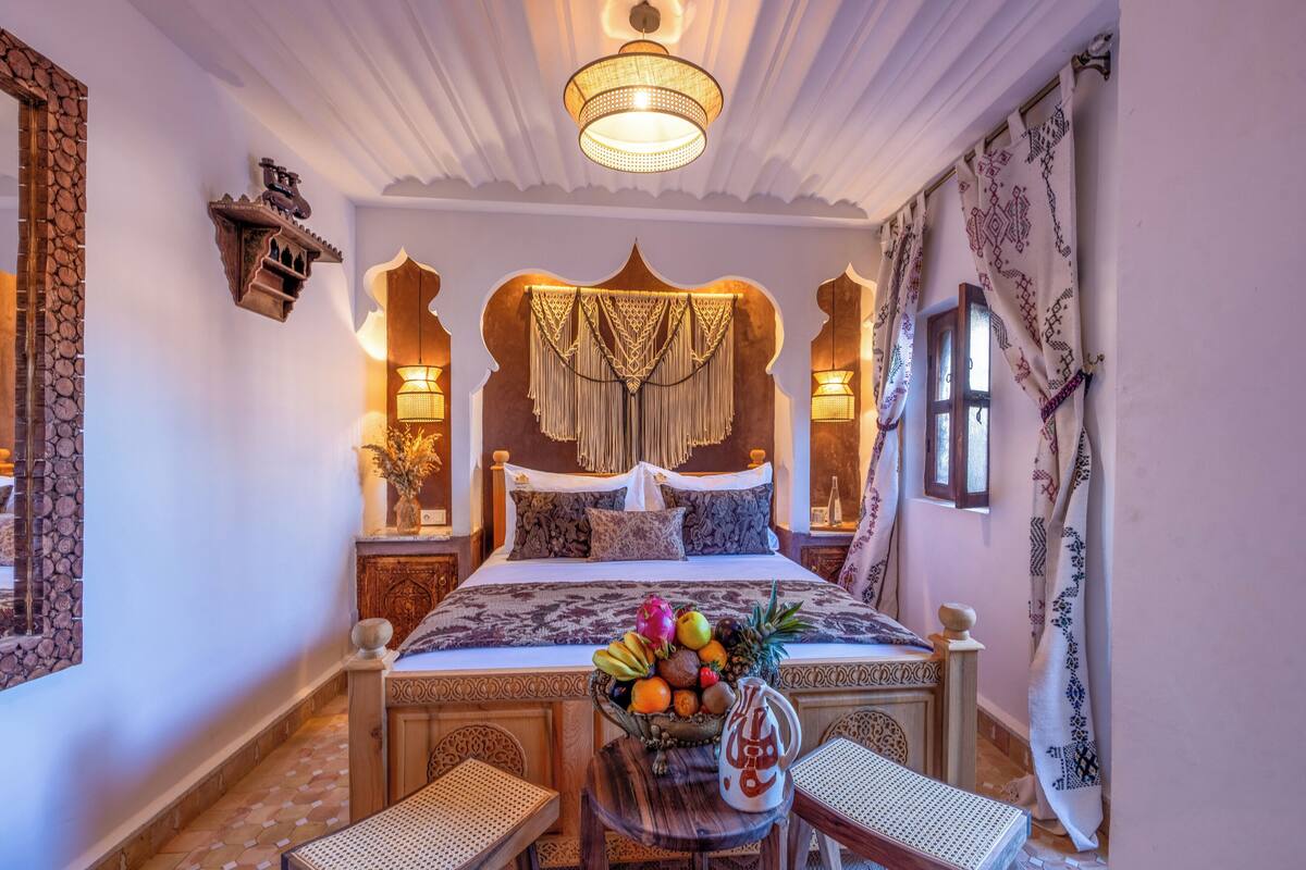 Un dormitorio con una cama grande, una araña, cortinas estampadas y un frutero en la mesita de noche.