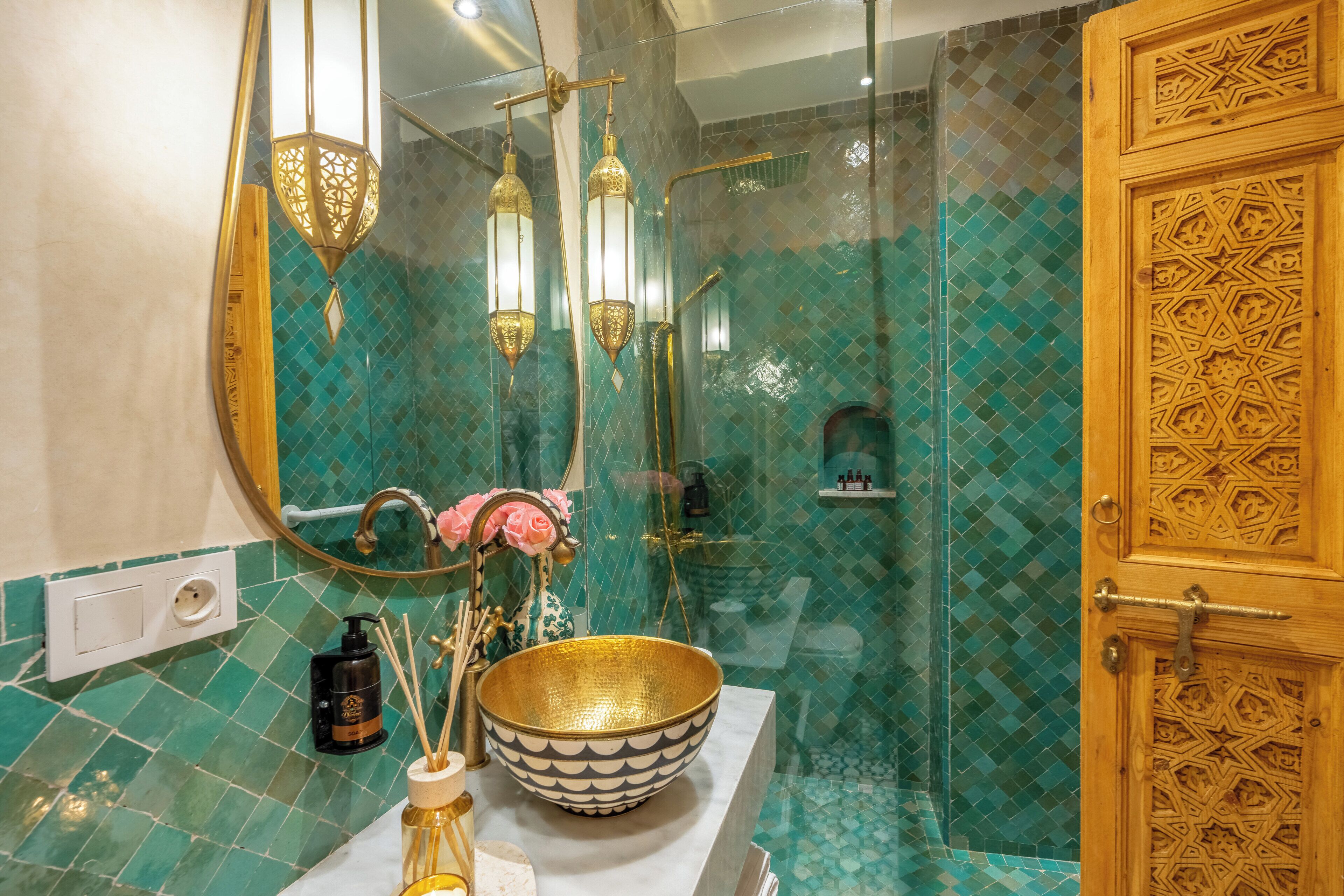 A bathroom with a large mirror, a gold bowl on the counter, and a shower with a glass door.
