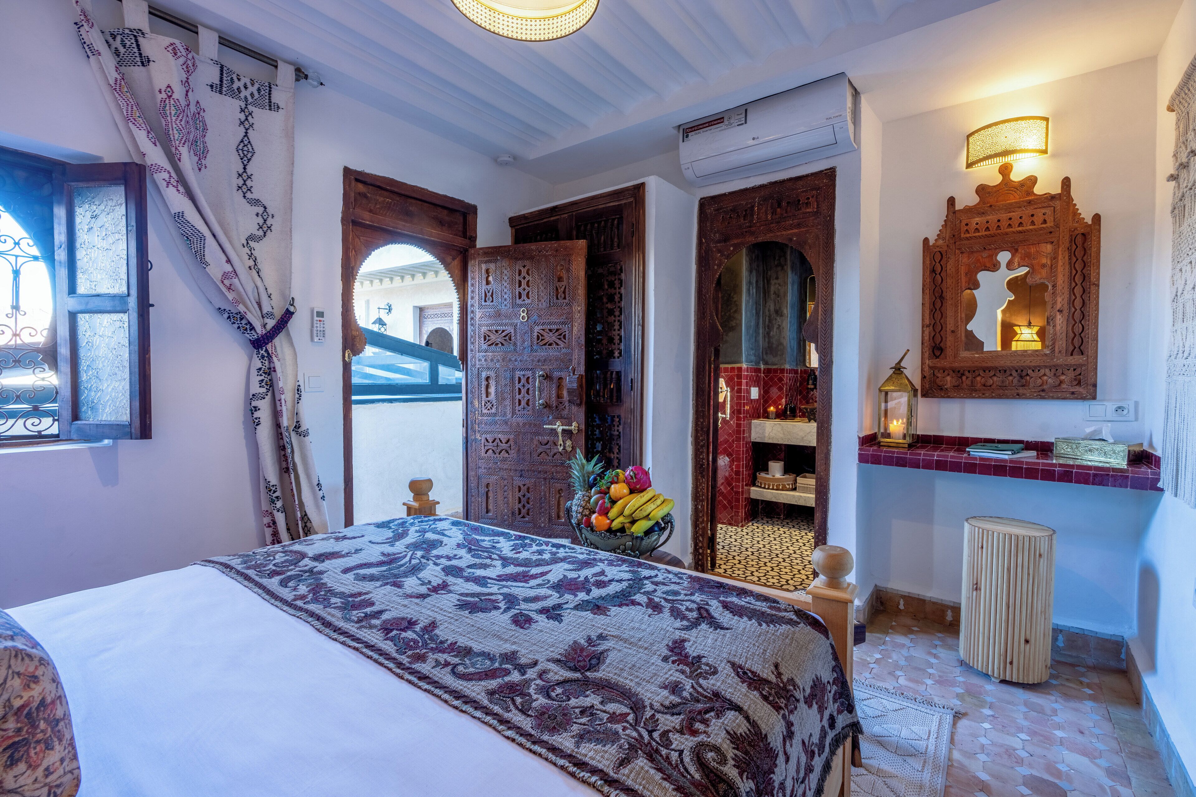 Una stanza con un letto, una porta in legno, uno specchio e un tavolino con una ciotola di frutta.