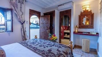 Una stanza con un letto, una porta in legno, uno specchio e un tavolino con una ciotola di frutta.