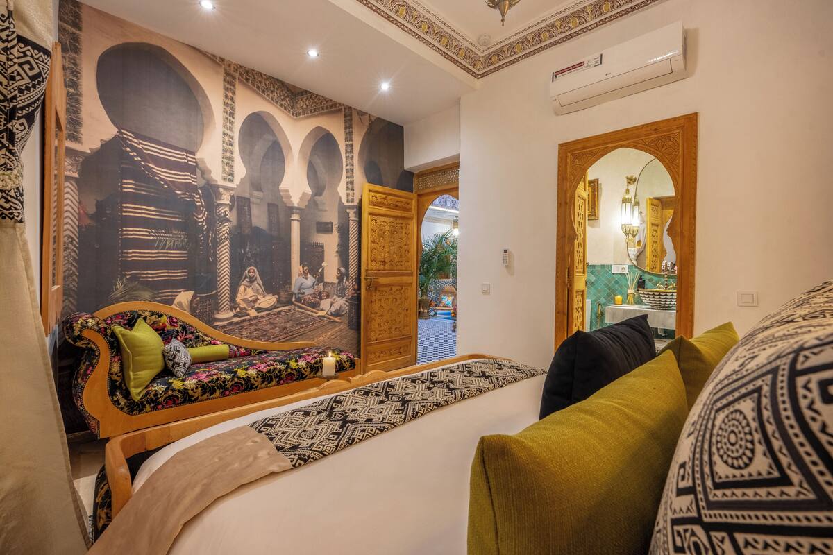 Un dormitorio con cama, sofá, un mural en la pared y un acceso a otra habitación.