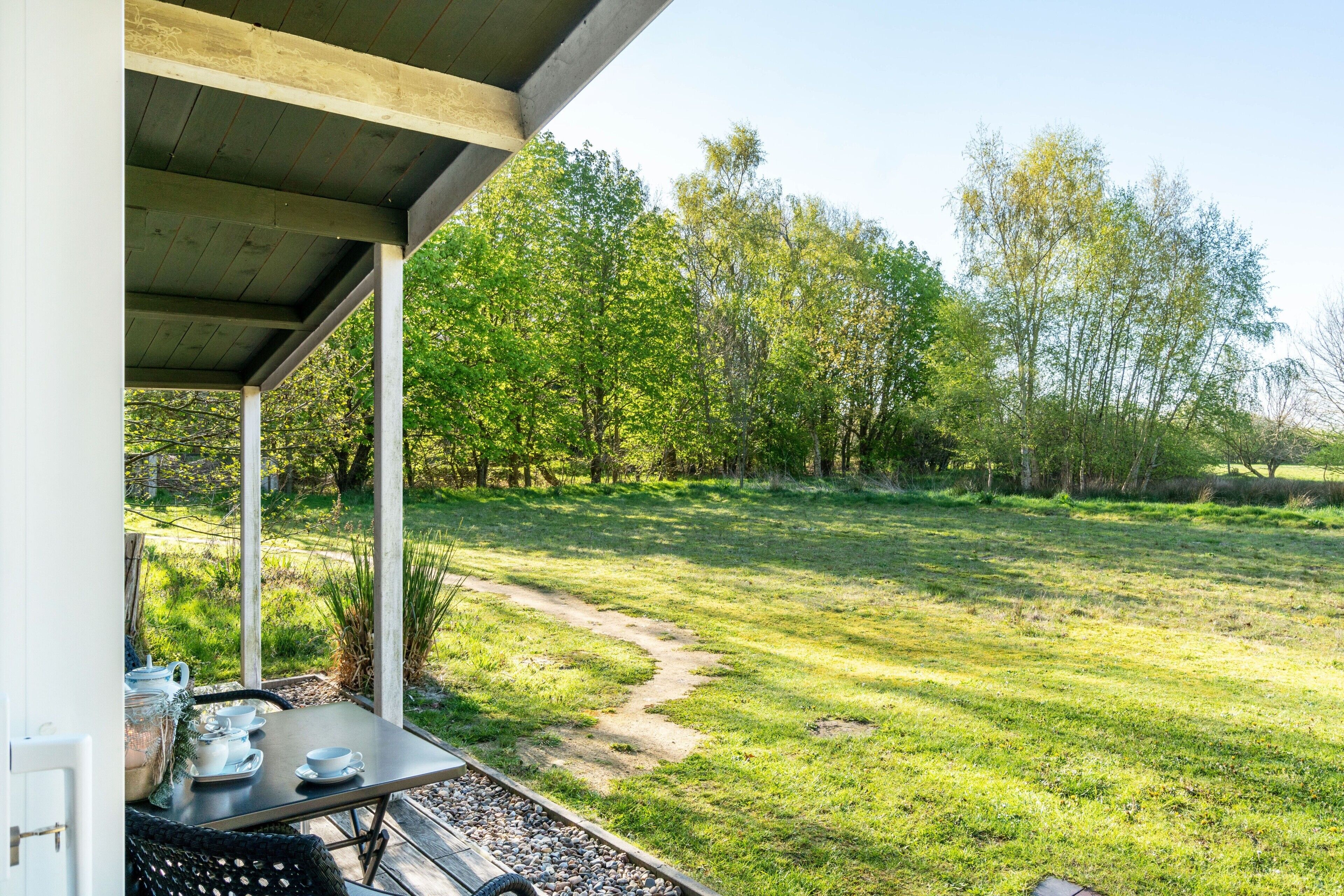 An outdoor patio with a table set for tea, surrounded by a grassy area with trees.