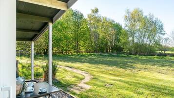 An outdoor patio with a table set for tea, surrounded by a grassy area with trees.