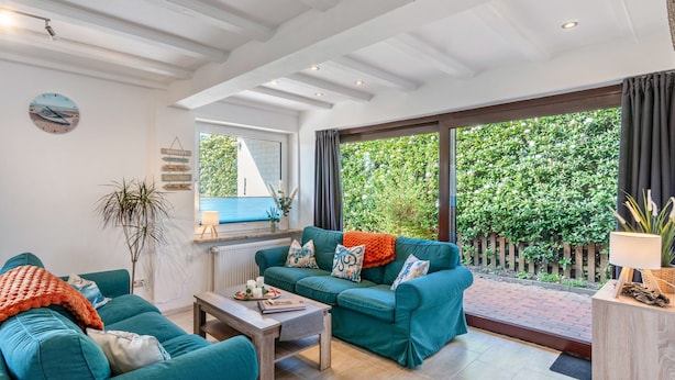A spacious living room with a large window, a cozy sofa set, and a wooden coffee table. - Holiday Home for 5 People (105 m²) in Südbrookmerland (Südbrookmerland)