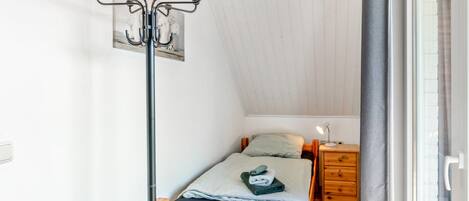 A small, cozy room with a wooden bed, a nightstand, a lamp, and a coat rack.