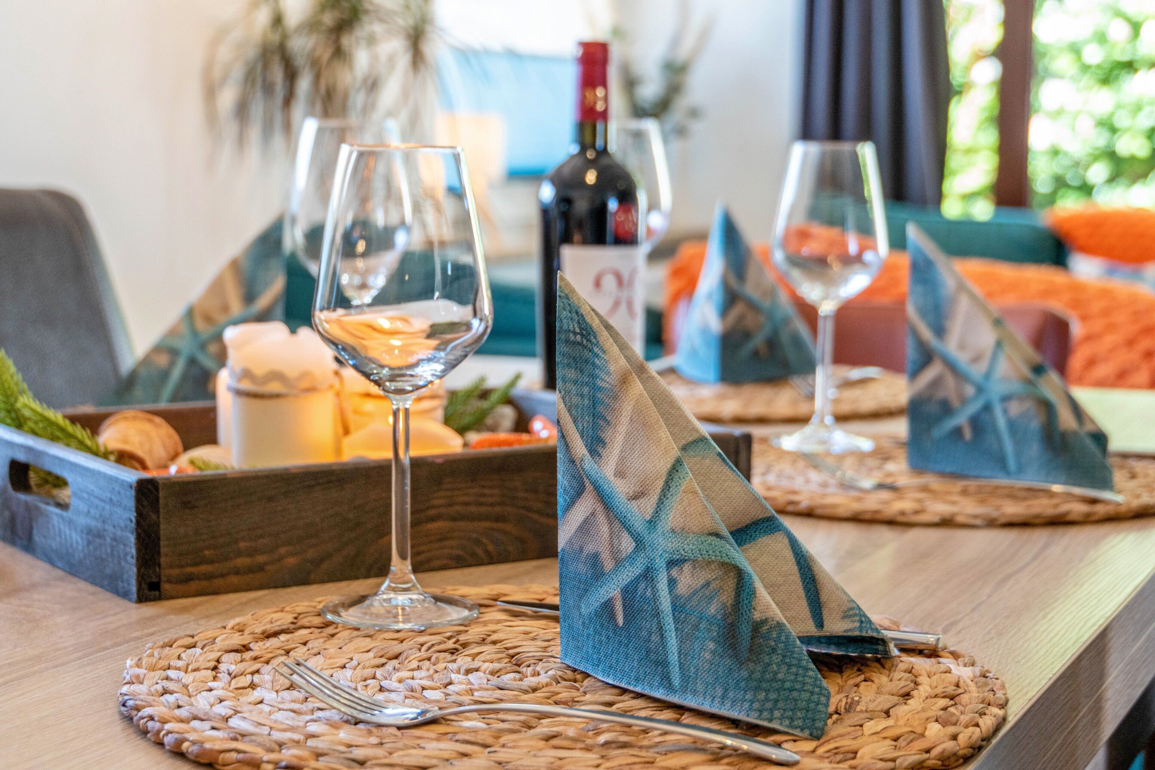Une table à manger avec des sets de table, des verres à vin, des couverts et une bouteille de vin.