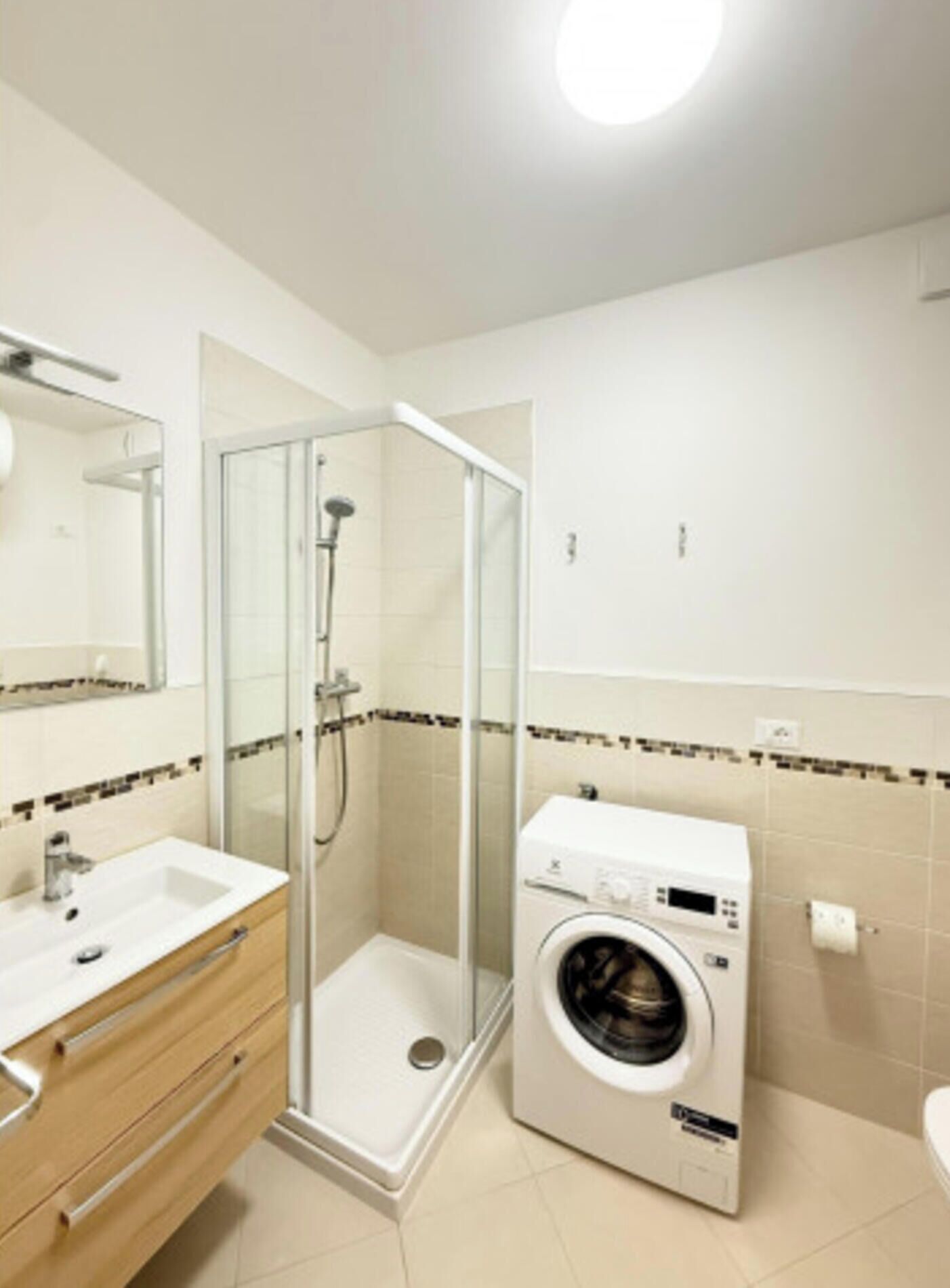 Une salle de bain moderne dotée d’une douche à parois de verre, d’un lave-linge encastré et d’un meuble-lavabo avec miroir.