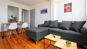 Un salon moderne avec un canapé d’angle gris, une table à manger en bois avec des chaises et une petite table d’appoint en bois agrémentée d’une plante.