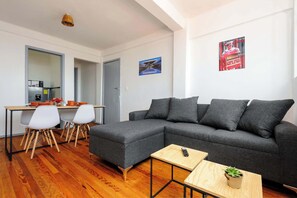 A modern living room with a grey sectional sofa, a wooden dining table with chairs, and a small wooden side table with a plant. - Edificio Aurora: Views & Vintage Charm (Centro)