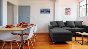 Un salon moderne avec un canapé d’angle gris, une table à manger en bois avec des chaises blanches et une petite table basse.