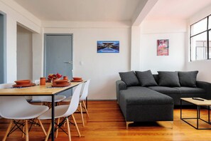 A modern living room with a grey sectional sofa, a wooden dining table with white chairs, and a small coffee table. - Edificio Aurora: Views & Vintage Charm (Centro)