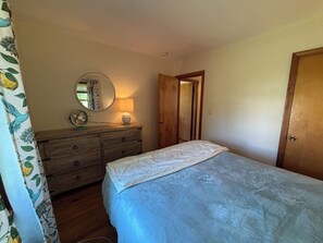 A bedroom with a bed, a dresser, a mirror, a lamp, and a door. - Iris Cottage-Walk to Short Sands (York)