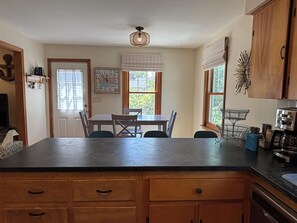 A kitchen with a dining table, chairs, a clock, and a coffee maker. - Iris Cottage-Walk to Short Sands (York)