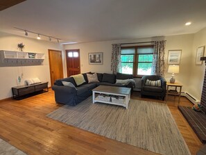 A living room with a sectional sofa, a coffee table, a bench, and a fireplace. - Iris Cottage-Walk to Short Sands (York)