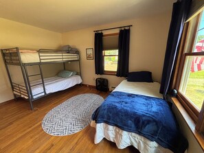 Habitació amb lliteres, un llit individual, finestra amb cortines, radiador i una catifa amb dibuixos.