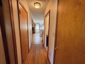 A hallway with wooden doors and a tiled floor, leading to a room with a television and a cart. - Iris Cottage-Walk to Short Sands (York)