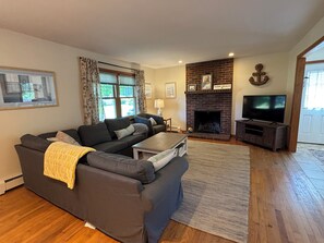 A living room with a sectional sofa, a fireplace, a television, and a framed picture on the wall. - Iris Cottage-Walk to Short Sands (York)