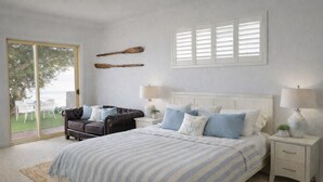 Une chambre à coucher comprenant un lit, une table de chevet, une lampe, une chaise et donnant sur l’extérieur.