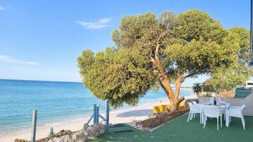 A seaside patio with a table and chairs, a tree, and a view of the ocean.