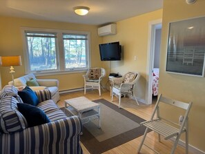 Un salón con sofá, sillas, televisión y ventana con vista a árboles.