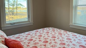 Un dormitorio con cama, dos ventanas y vistas al exterior con árboles y agua.