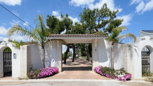 A gated entrance with a covered walkway, surrounded by flowering plants and trees. - Apartment 'Casa Torre Di Specchio with Pool' – Wi-Fi and Air Conditioning (Bari)
