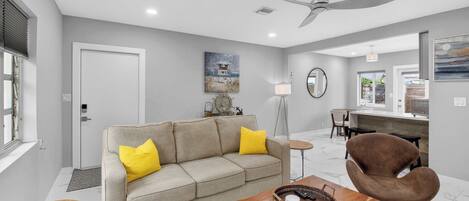 A modern living room with a sofa, coffee table, and chairs, a ceiling fan, and artwork on the walls.