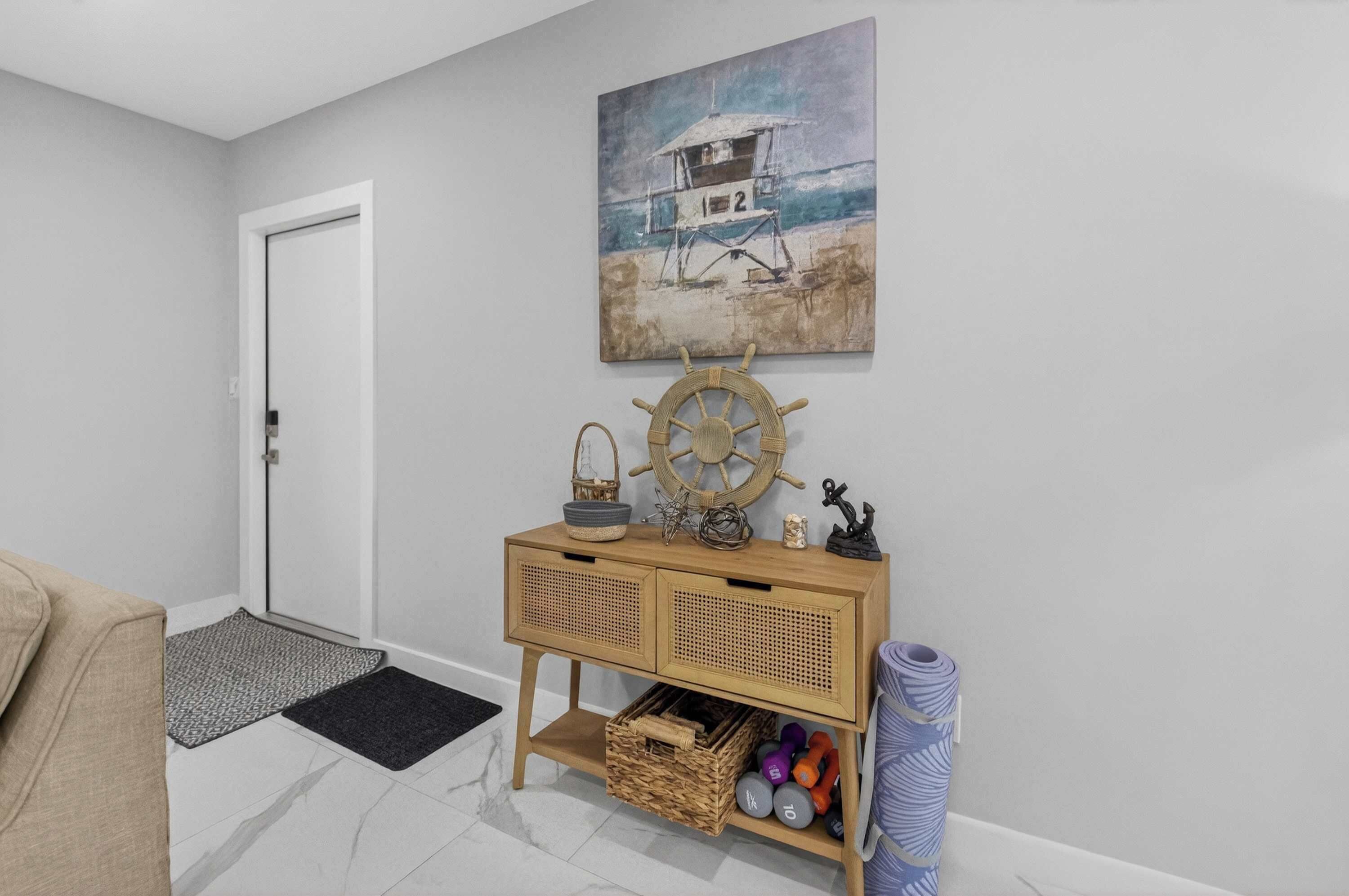 A hallway with a wooden console table, a ship's wheel, a lifeguard tower painting, and a door.