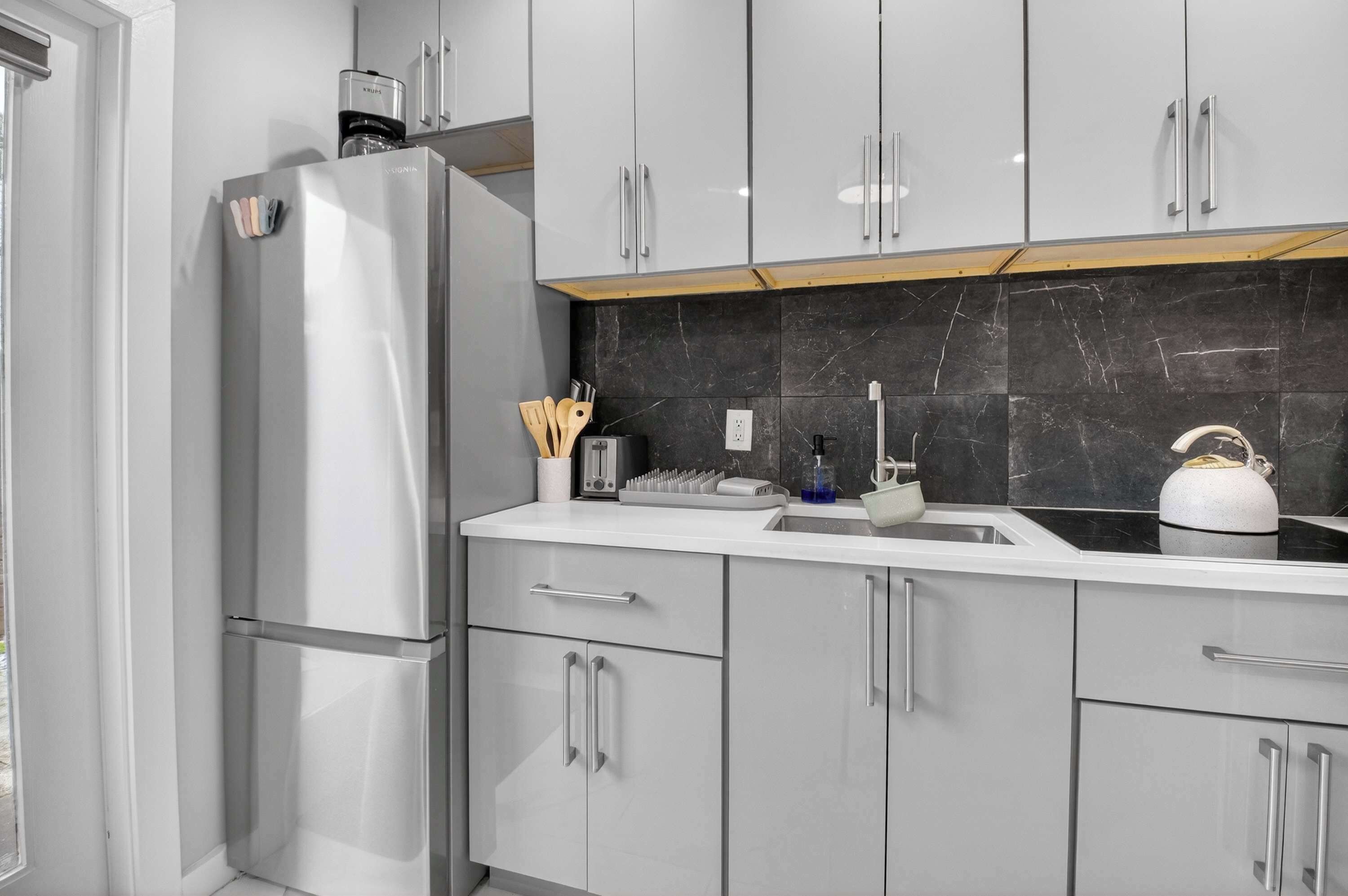 A modern kitchen with a stainless steel refrigerator, white cabinets, a marble backsplash, and a gas stove.