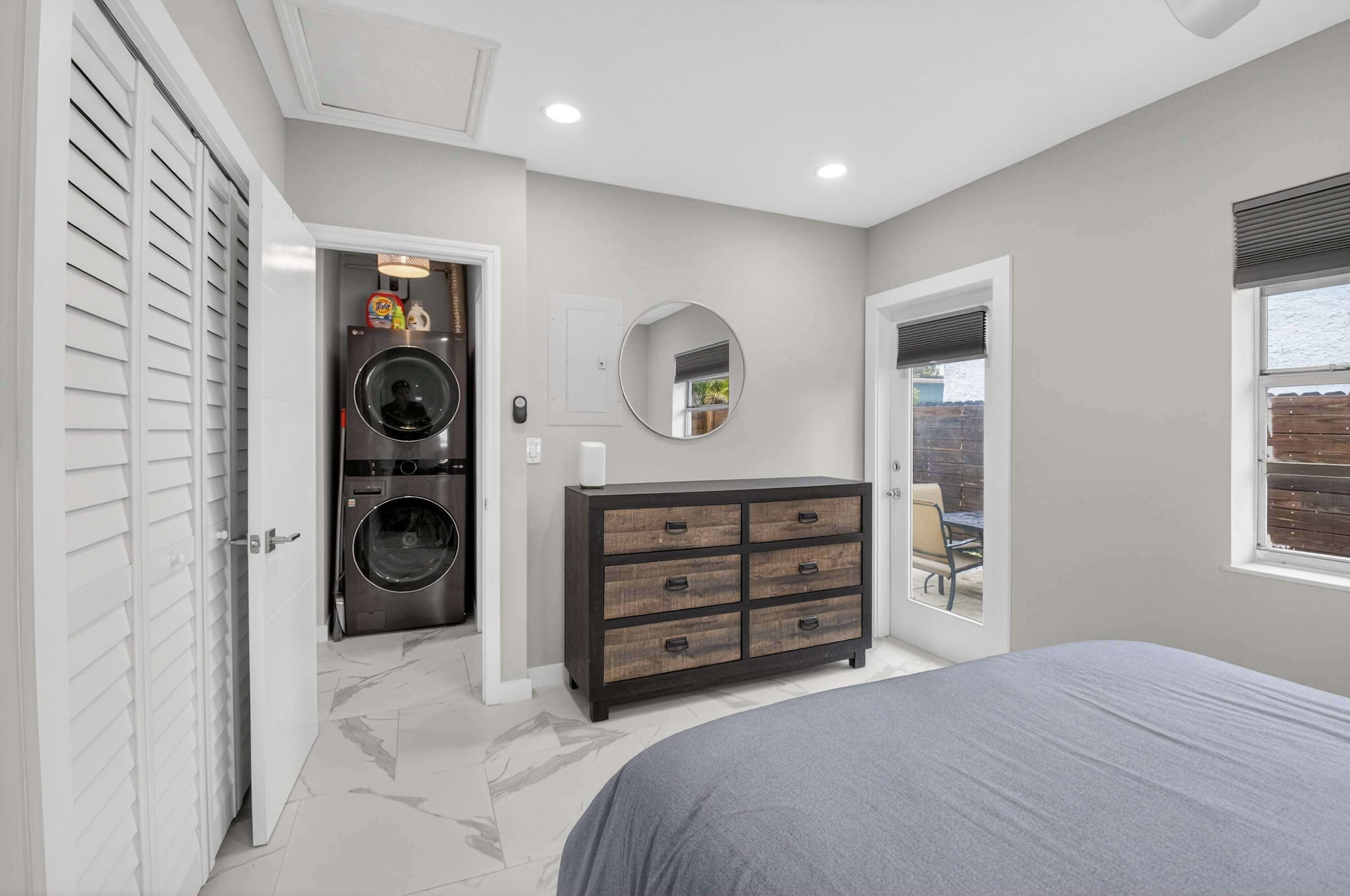 A bedroom with a bed, a dresser, a washing machine, and a mirror.