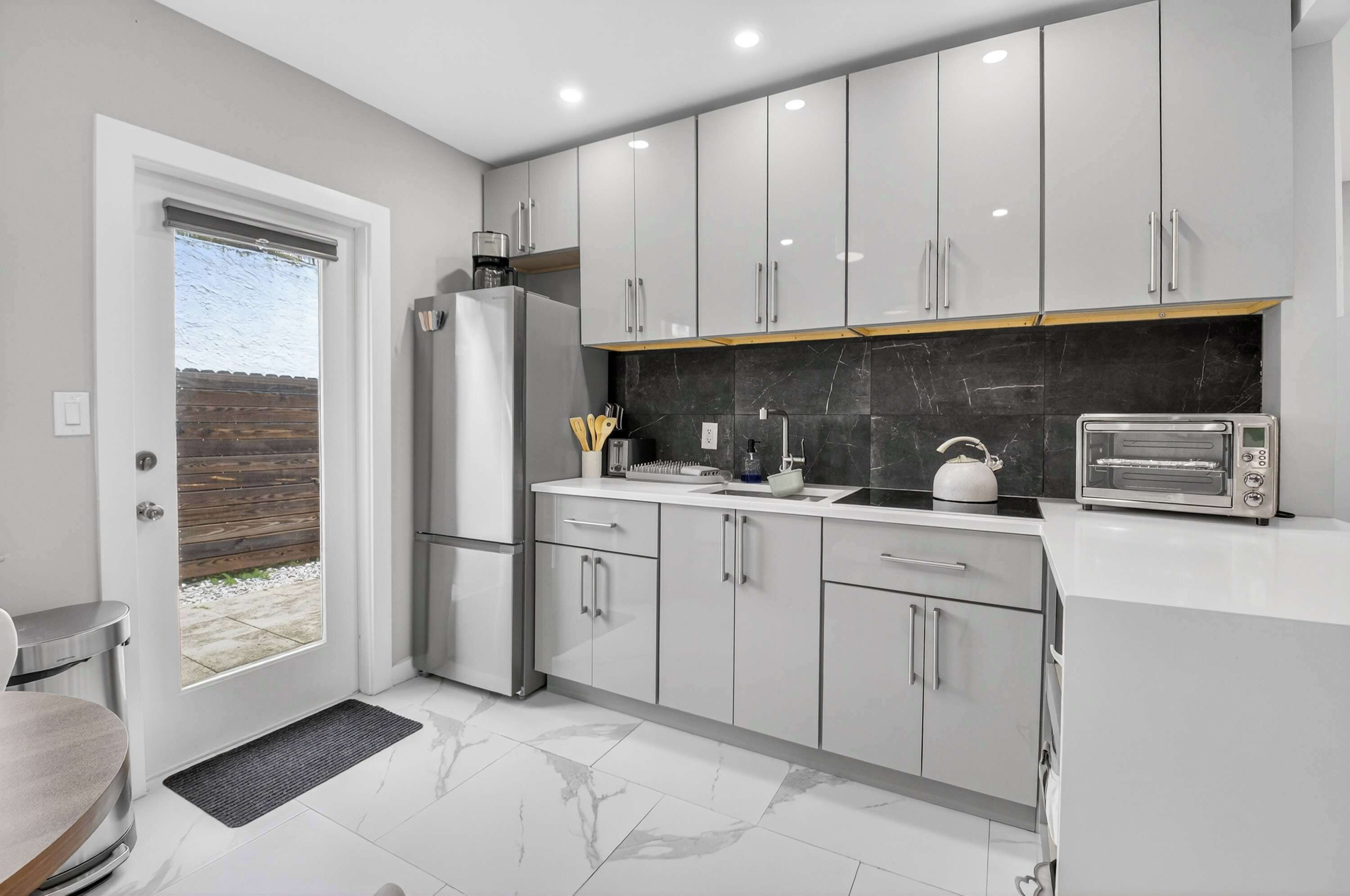 A modern kitchen with white cabinets, a black backsplash, a built-in oven, and a toaster.