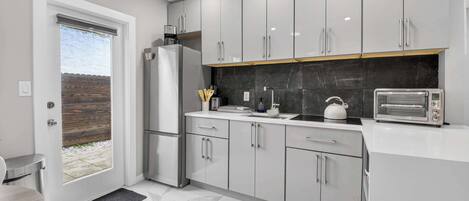 A modern kitchen with white cabinets, a black backsplash, a built-in oven, and a toaster.