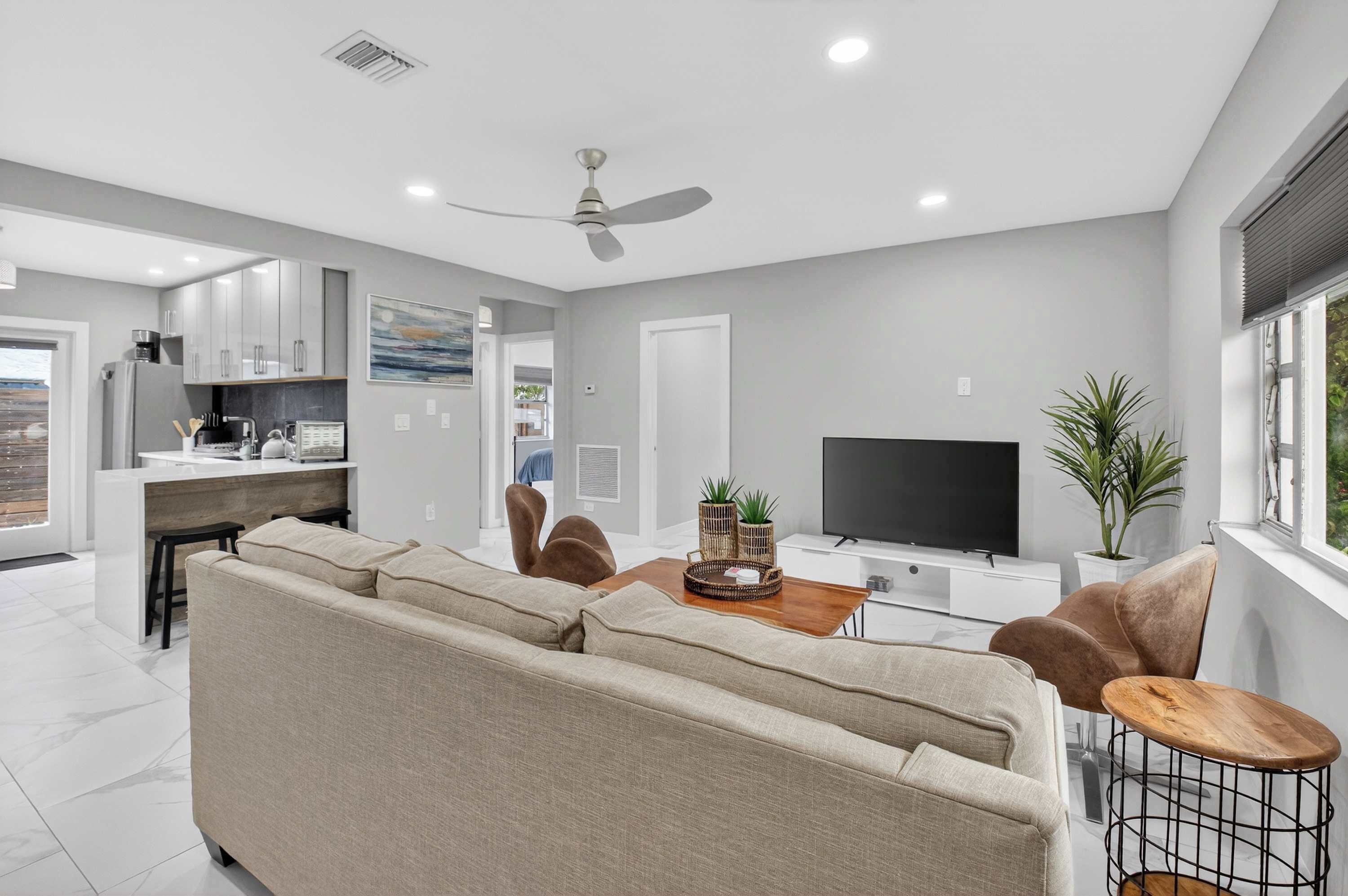 A modern living room with a sofa, coffee table, TV, and a dining area with chairs and a plant.