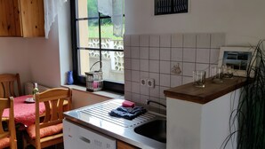 Uma cozinha com janela, pia, escorredor de louça e área de refeições com cadeiras e mesa.