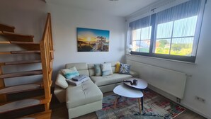 A modern living room with a sofa, a coffee table, a staircase, and a large window. - Apartment 'Haus Rose 2' with Shared Garden, Balcony and Wi-Fi (Loddin)